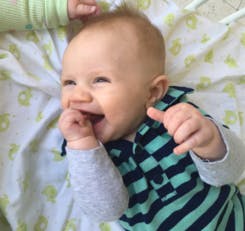 Child lying down, smiling with hand near mouth