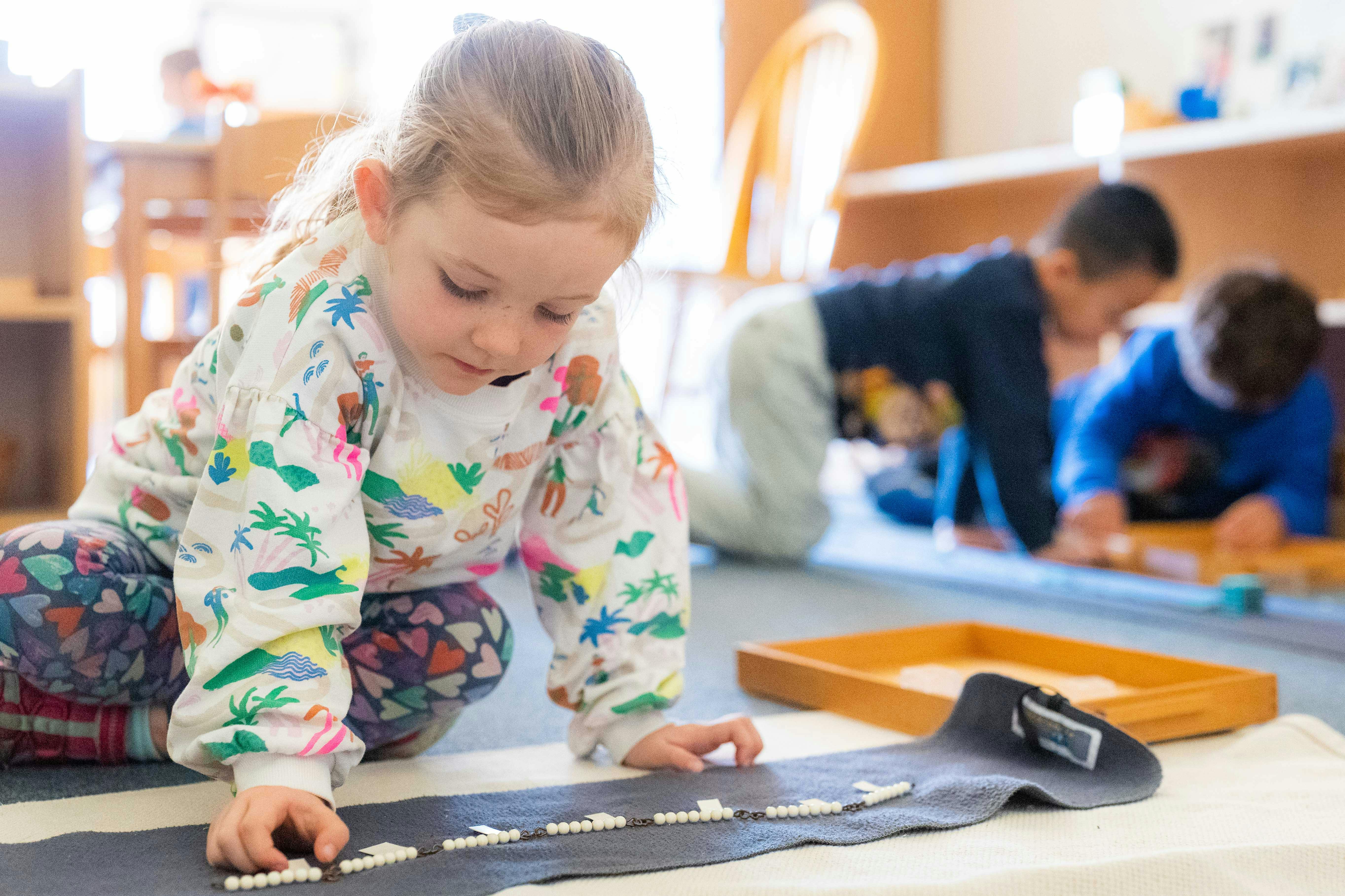 Child on floor arranging small white beads on a dark mat