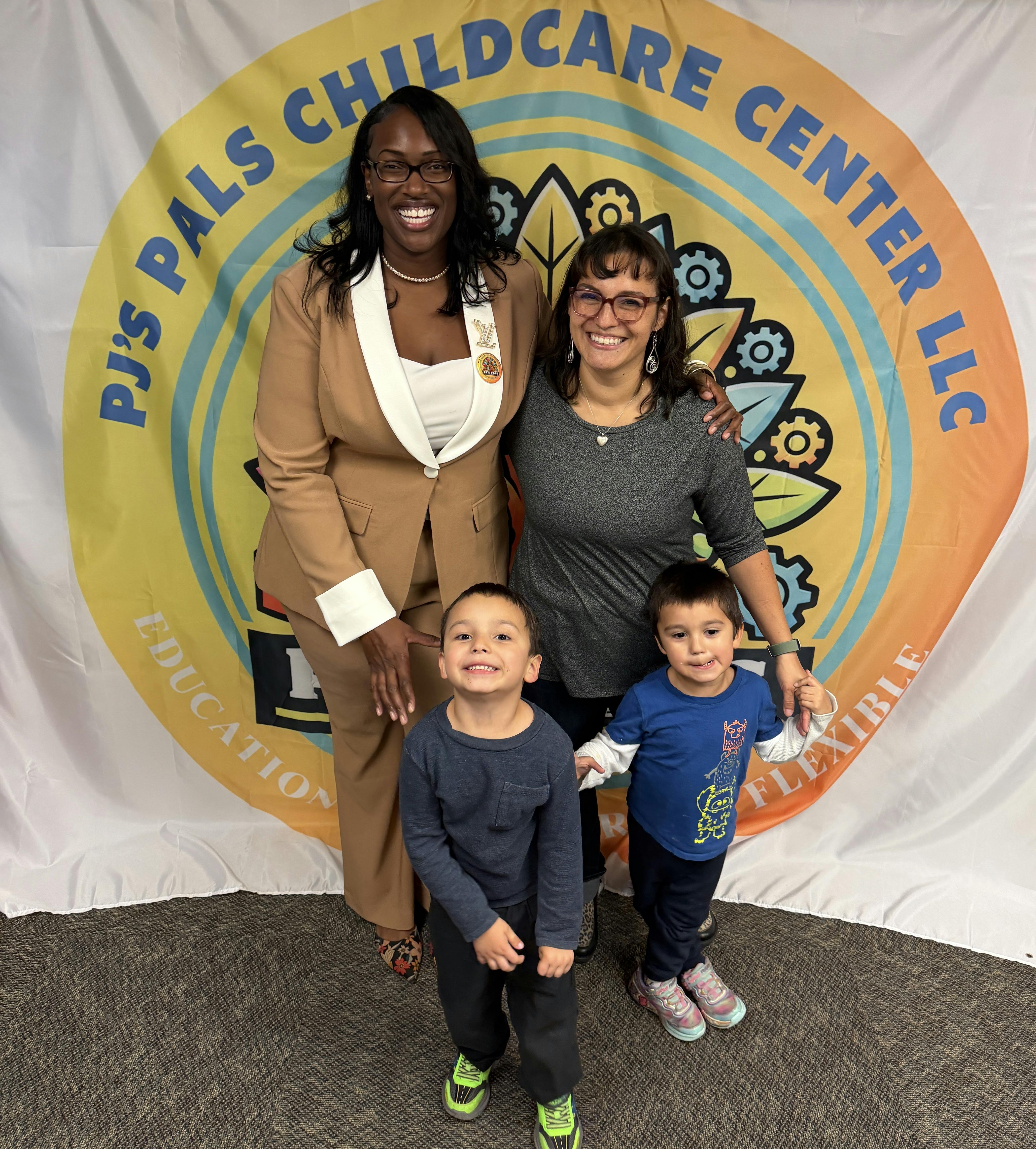 Two adults and two children posing in front of a childcare center banner