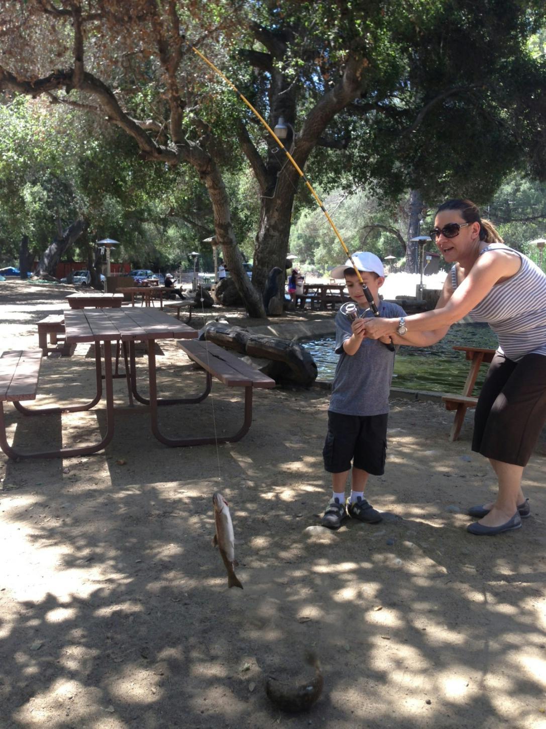 Person helping a child fish, with a fish on the line