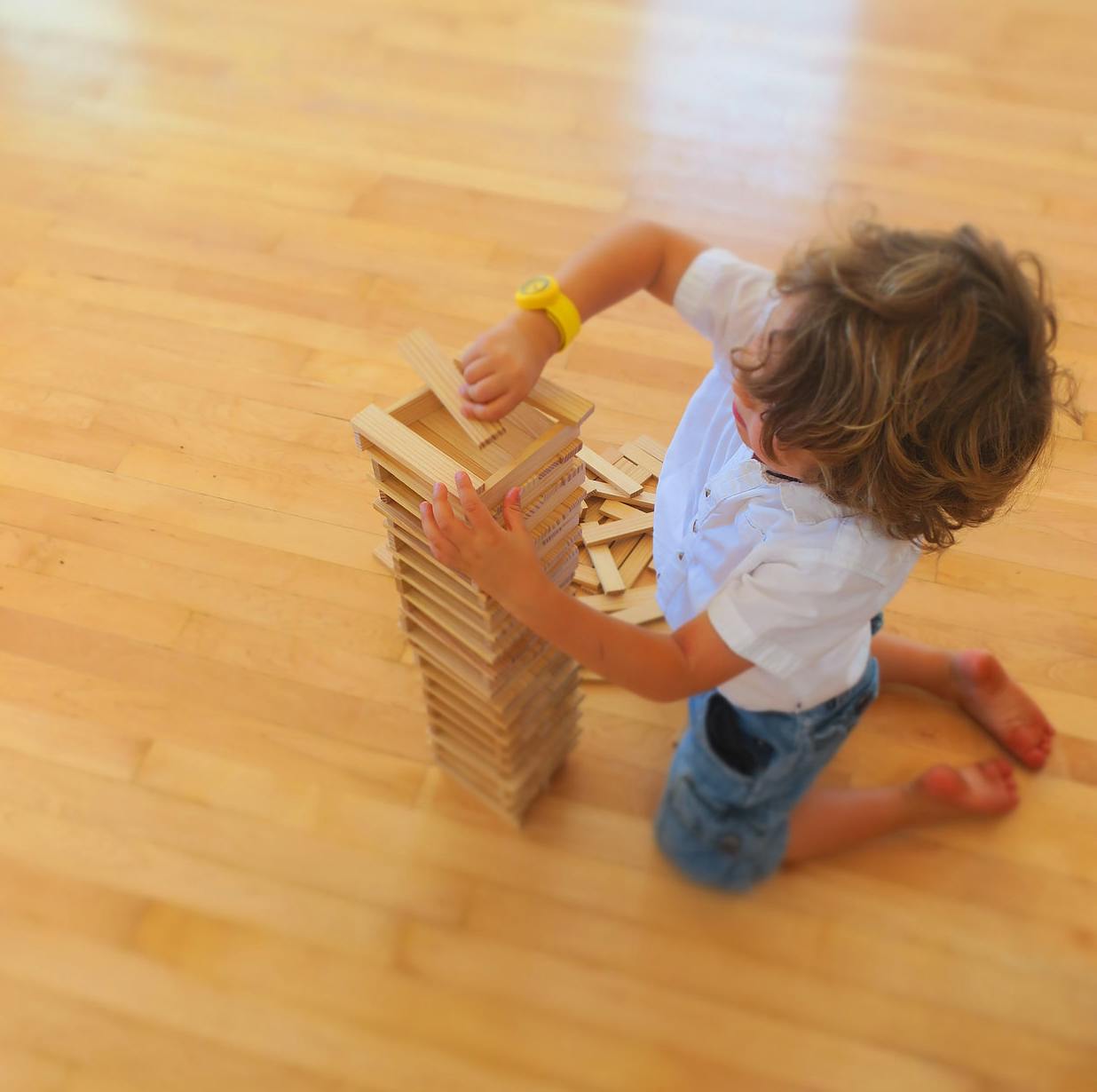Child kneeling on floor building a tower with wooden blocks