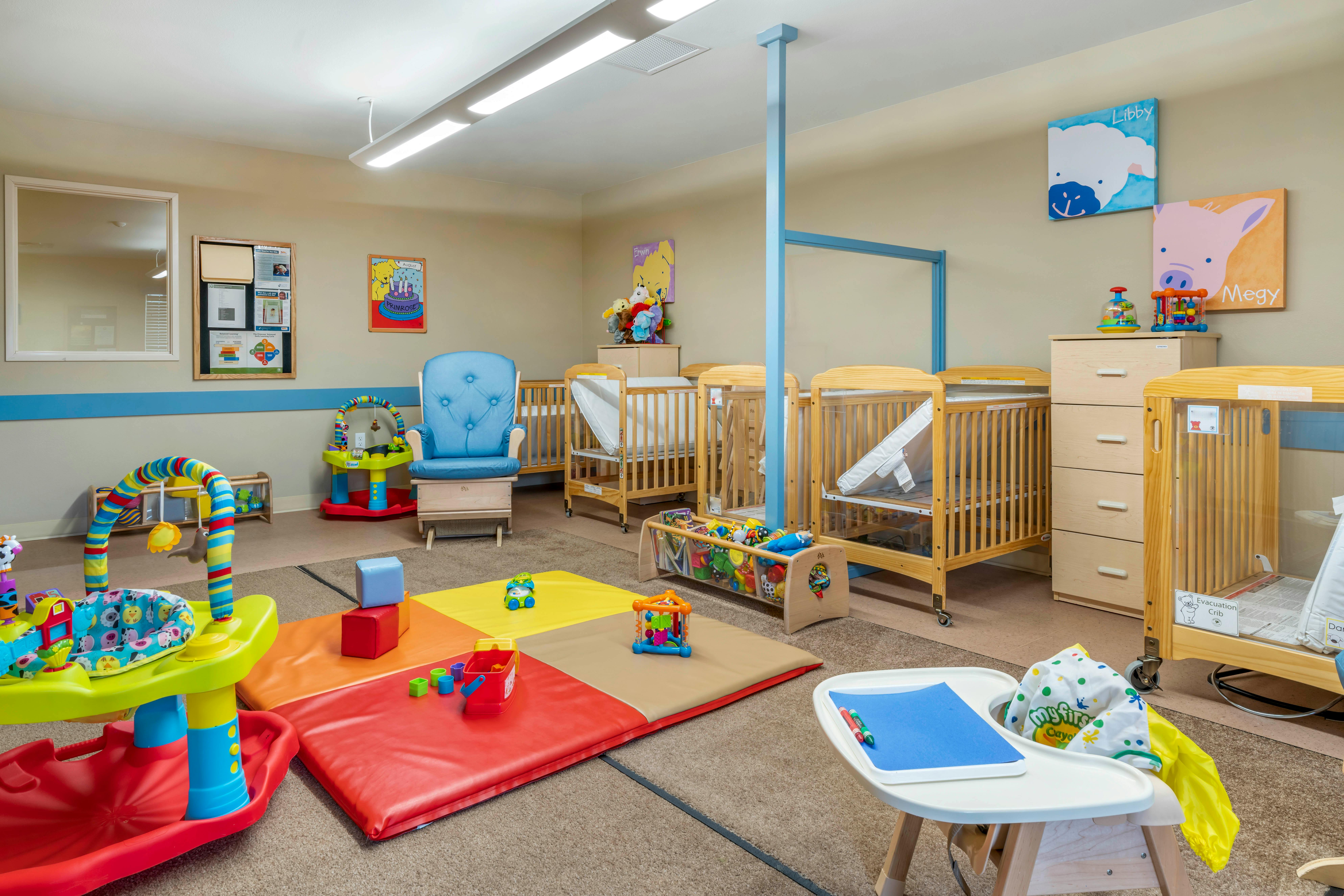 A colorful room in a daycare with cribs, playmats, and toys