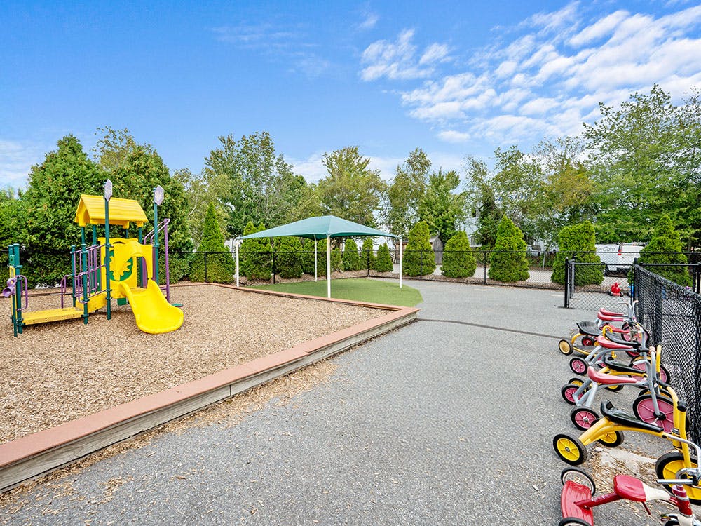 Playground with a yellow slide and a row of tricycles next to a fence