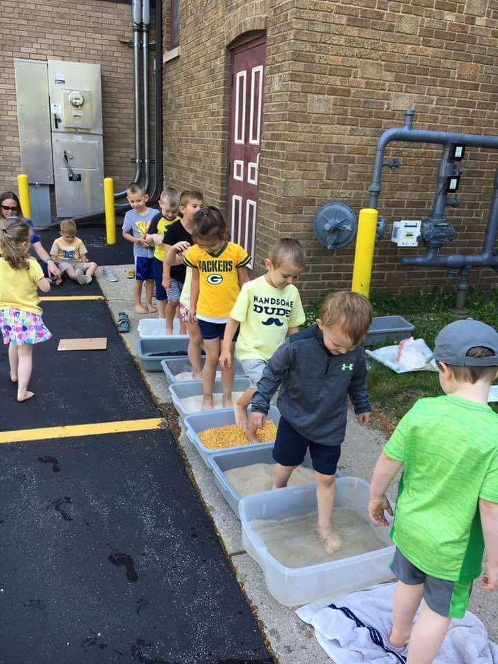 Children walking barefoot through sensory bins outdoors