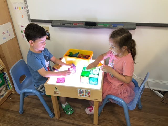 Two children playing with colorful blocks on a light table