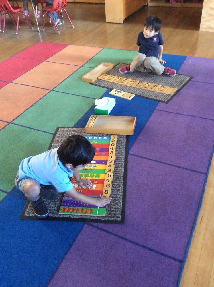 Two children playing with learning materials on a colorful rug