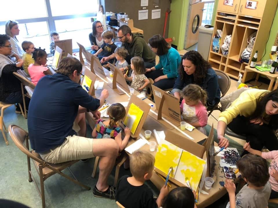 Adults and children painting at tables in a classroom