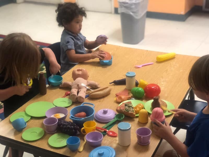 Three children playing with toy food and dishes at a table