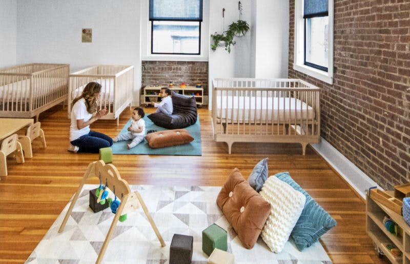 Adult and child playing on a rug in a room with cribs