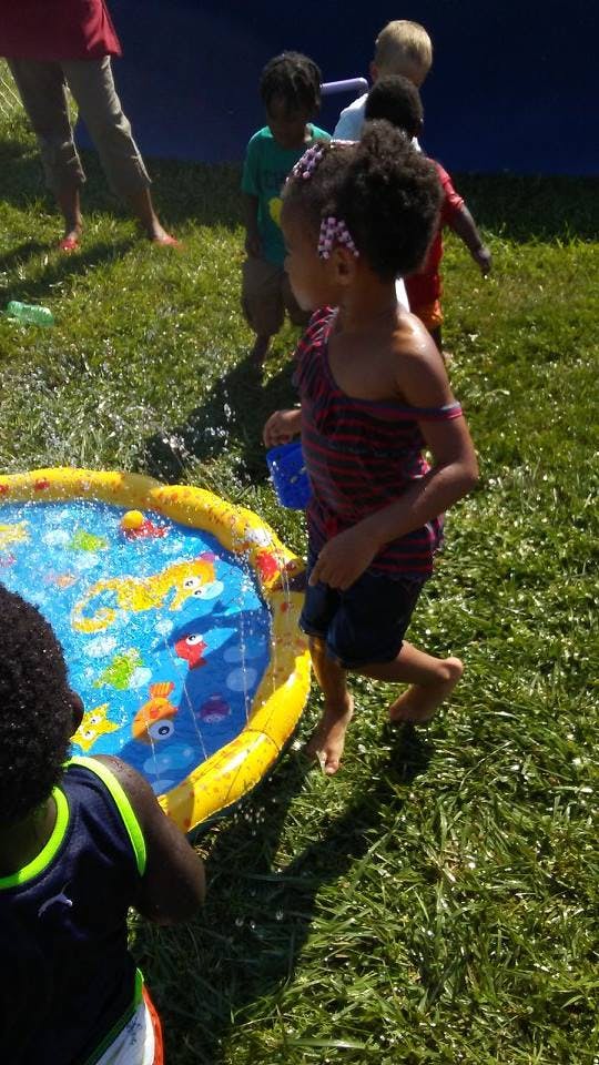 Children playing with a yellow and blue splash pad on grass