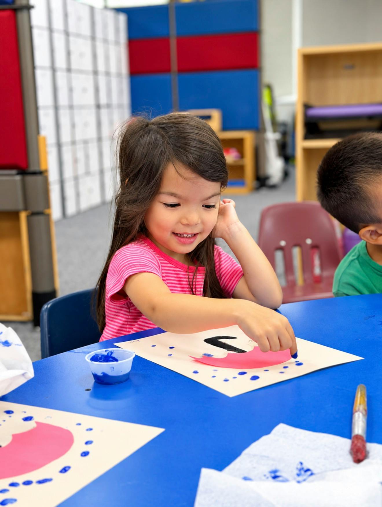 Child painting a paper craft at a table in a classroom