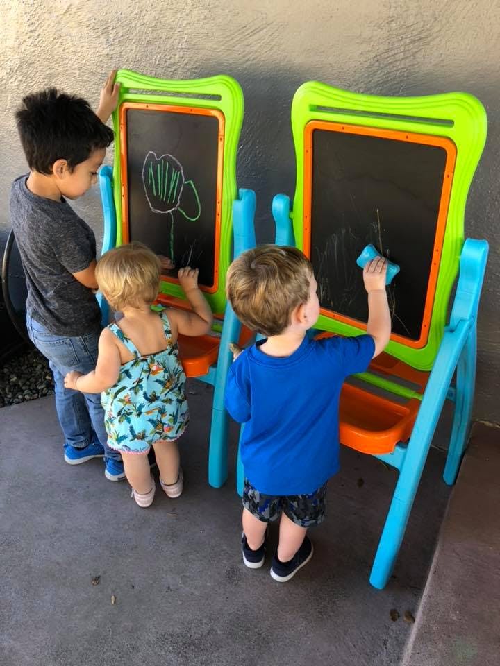 Three children drawing and erasing on two chalkboards