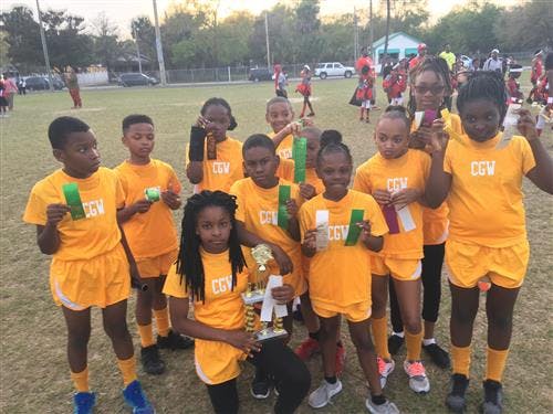 Group of children in yellow uniforms holding awards and a trophy on a field