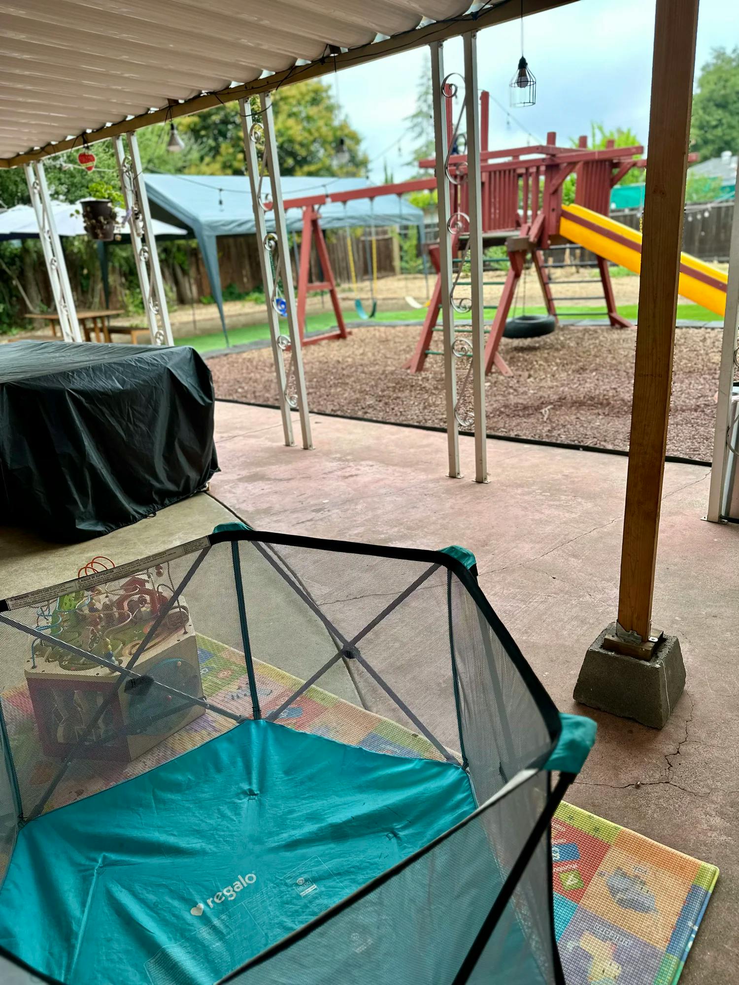 Playpen on a patio with a playground in the background