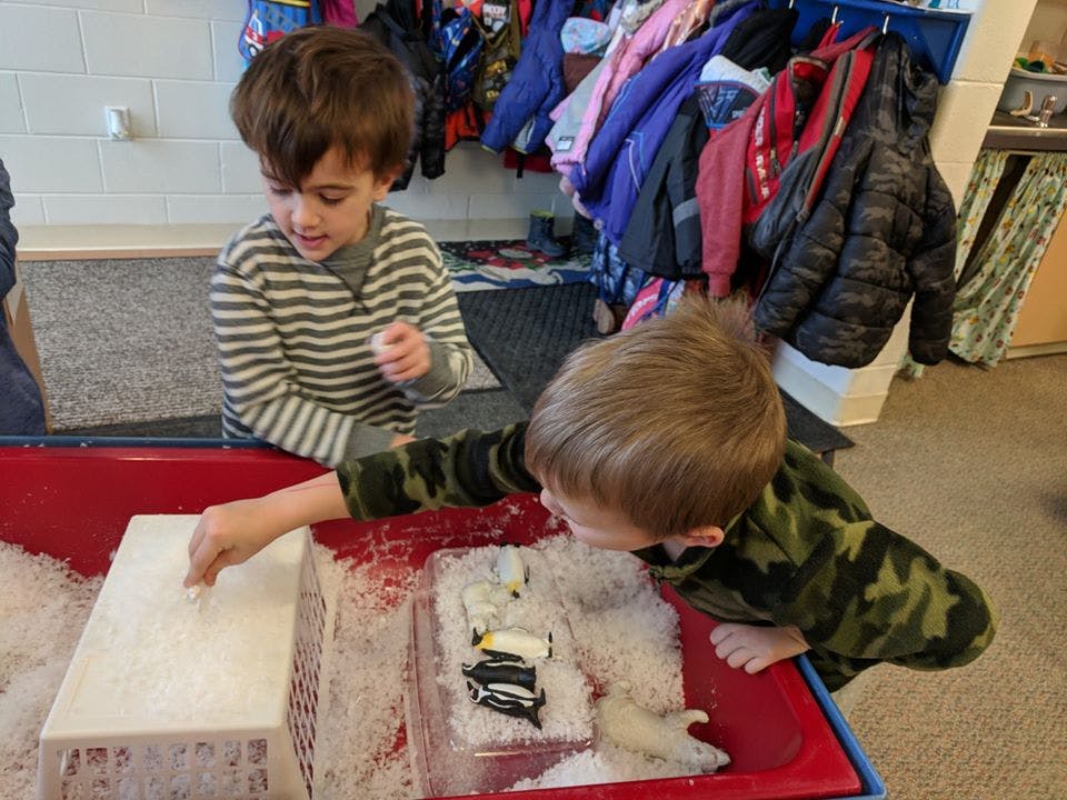 Two children playing with snow and toys in a red bin