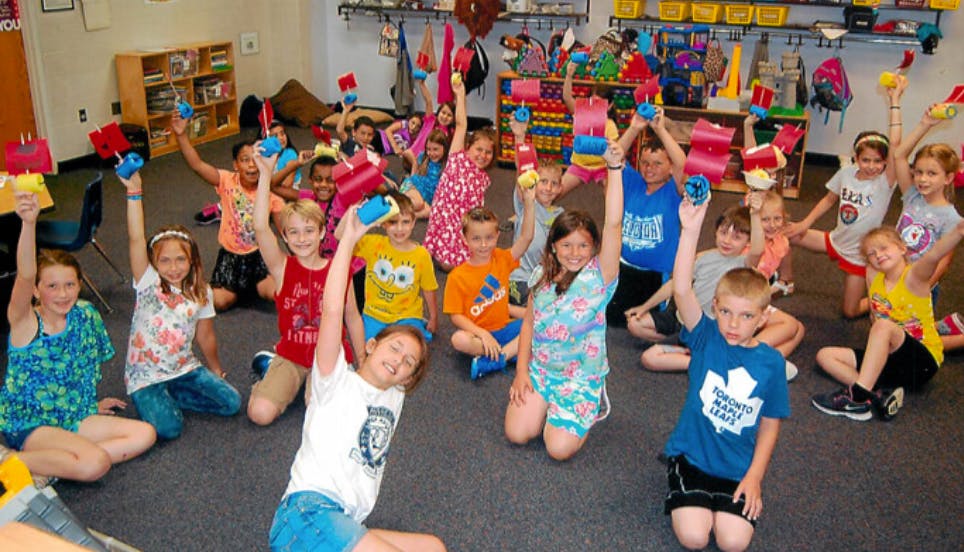 Group of children sitting on floor with arms raised holding objects
