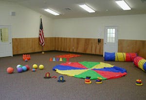 Indoor room with colorful play parachute, balls, and play tunnel