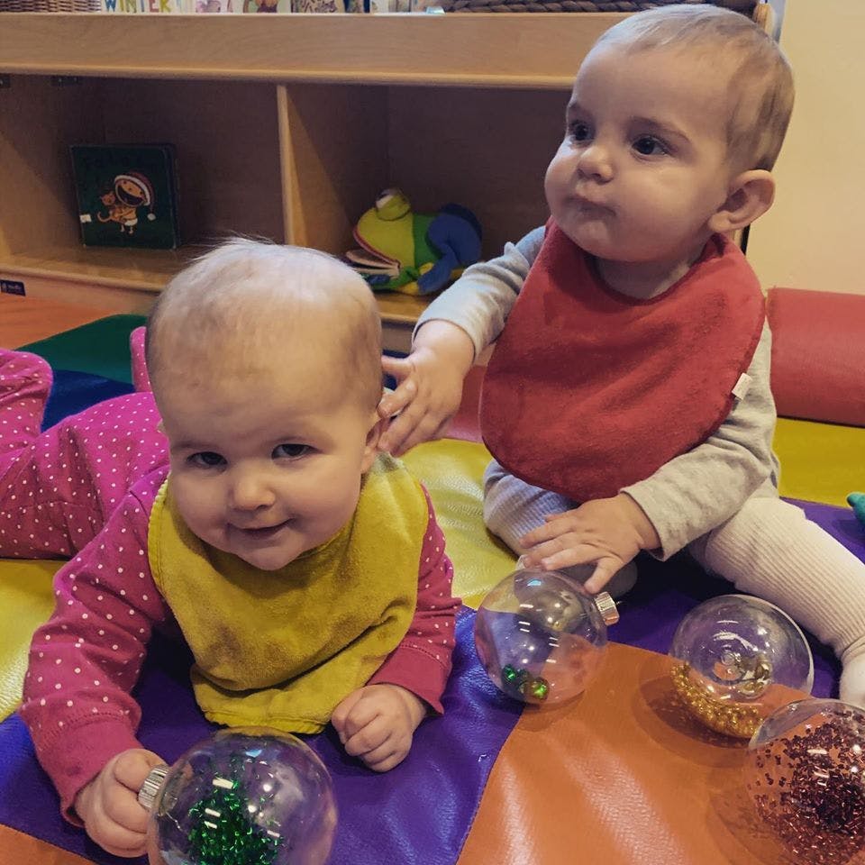 Two babies playing with clear plastic balls on a colorful mat