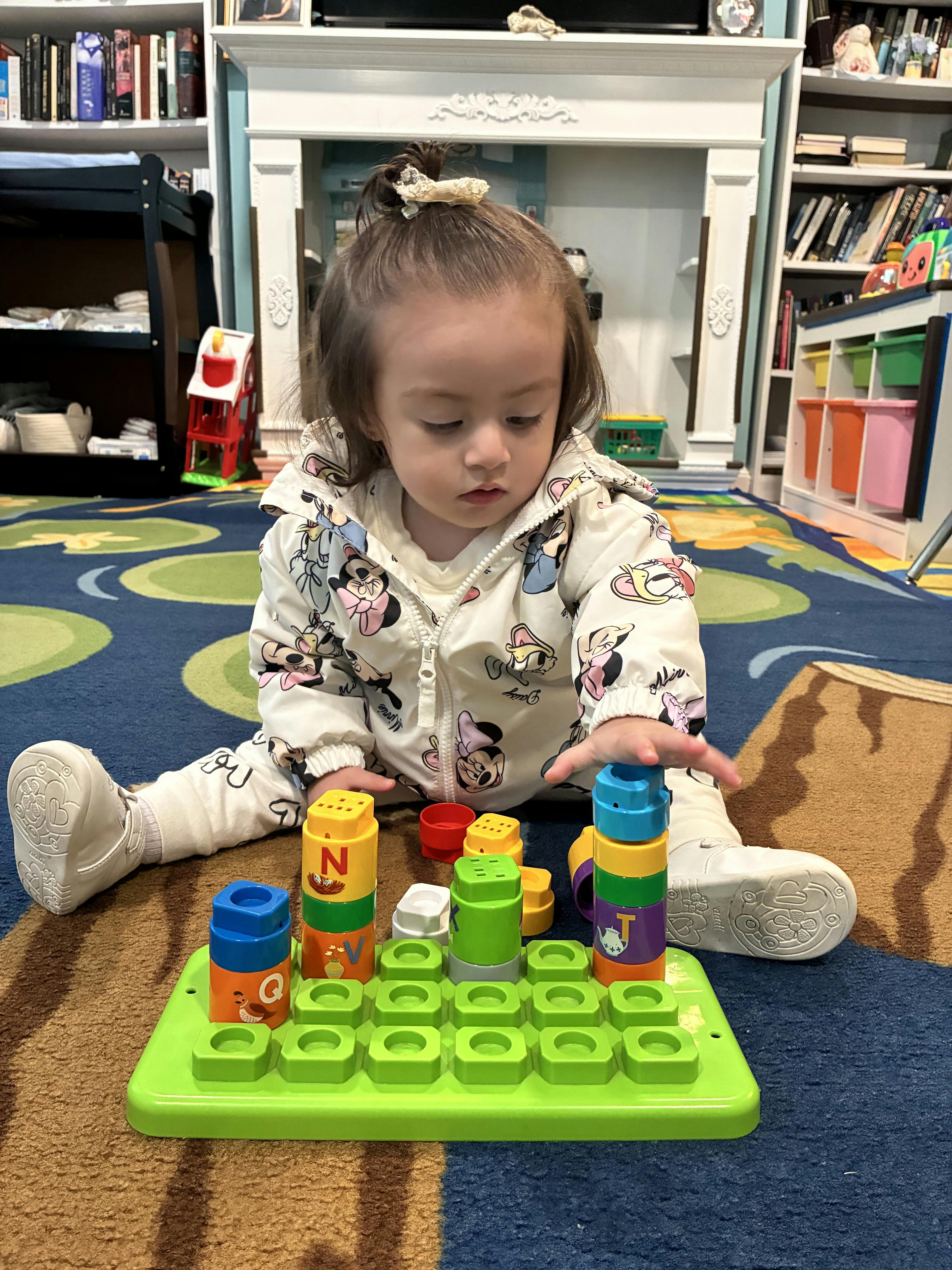 Child sitting on a patterned rug playing with colorful letter stacking blocks