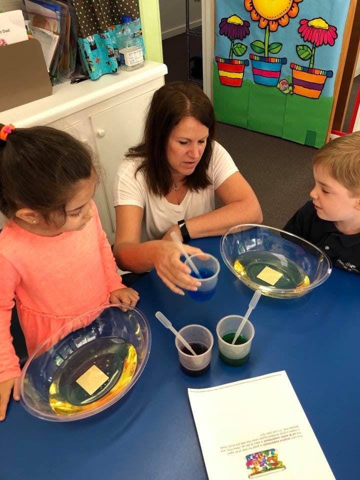 Adult and two children at a table with bowls of colored liquid and droppers