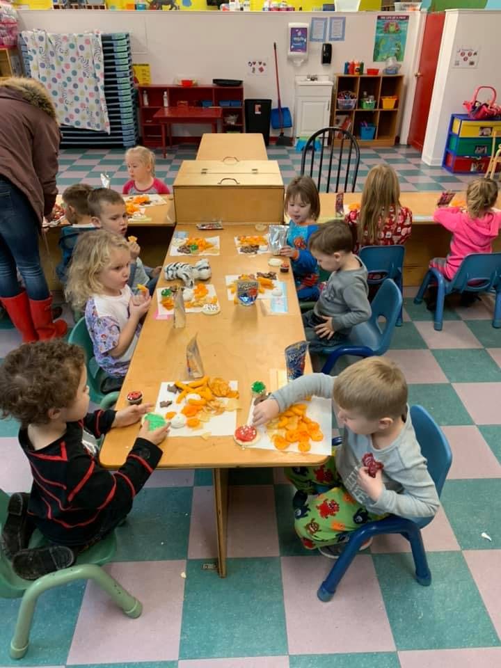 Children at tables in a classroom engaged in an activity with orange objects