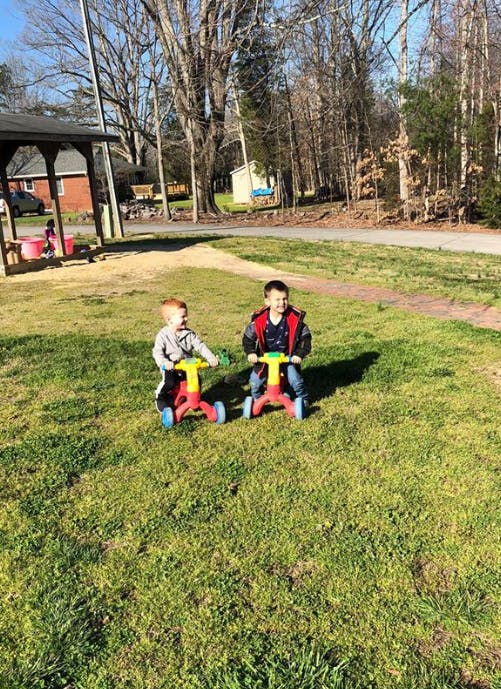 Two children riding tricycles on grass
