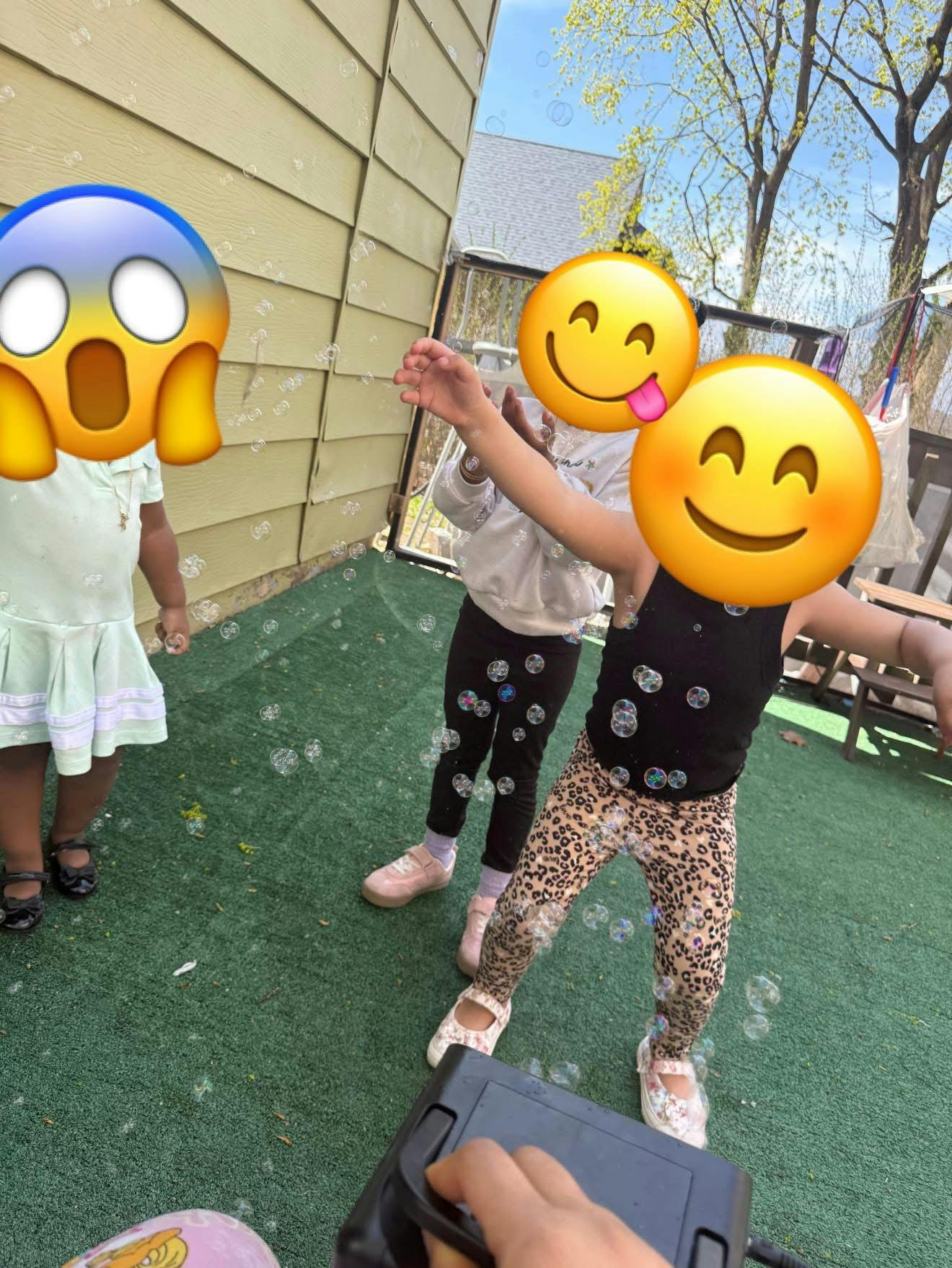 Three children playing with bubbles on green turf