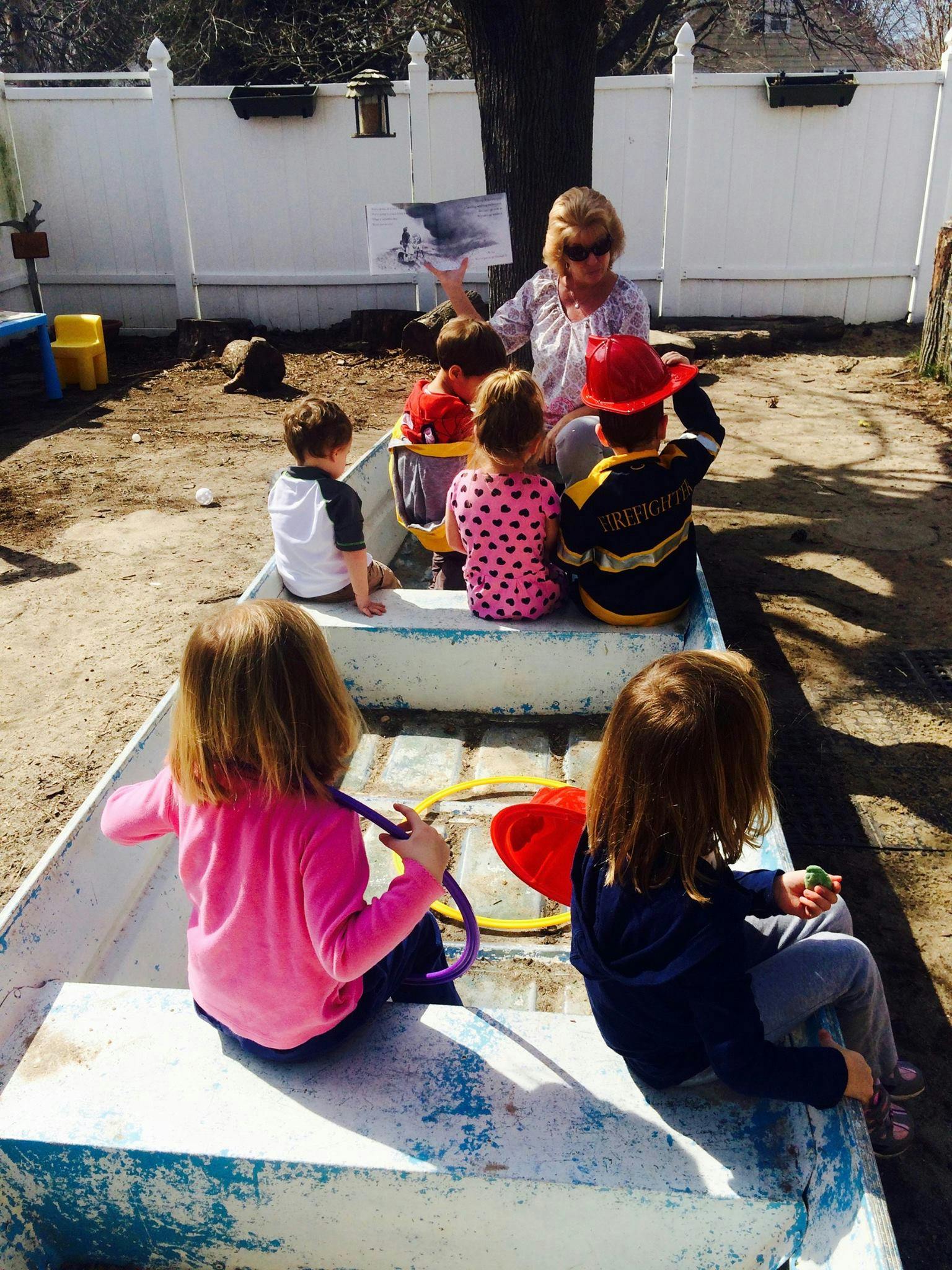 Adult reading to children in a boat-like structure outdoors