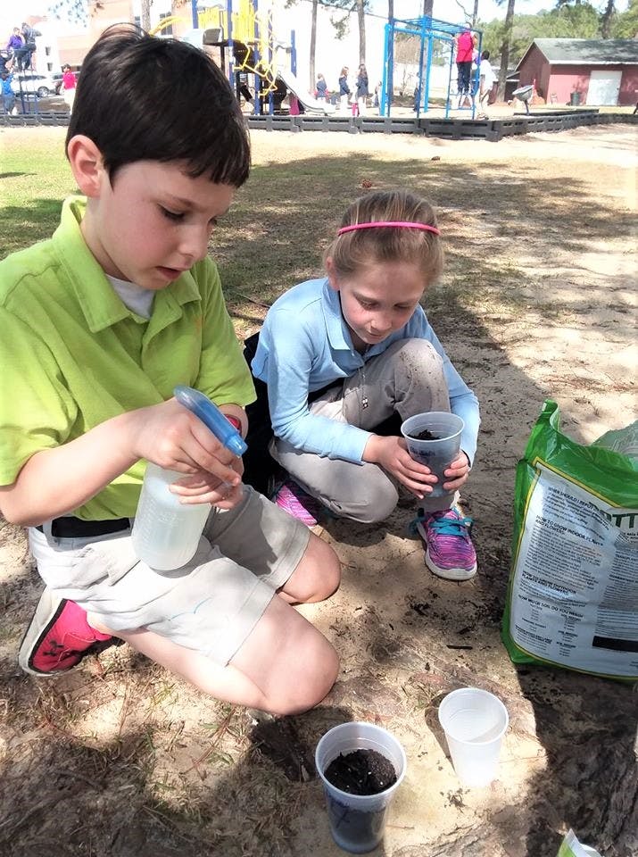 Two children planting in cups outdoors