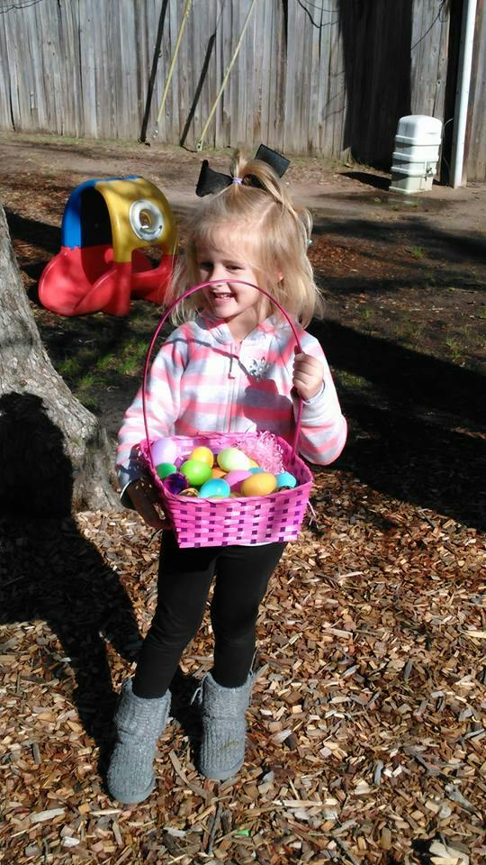Child holding a pink basket filled with colorful eggs