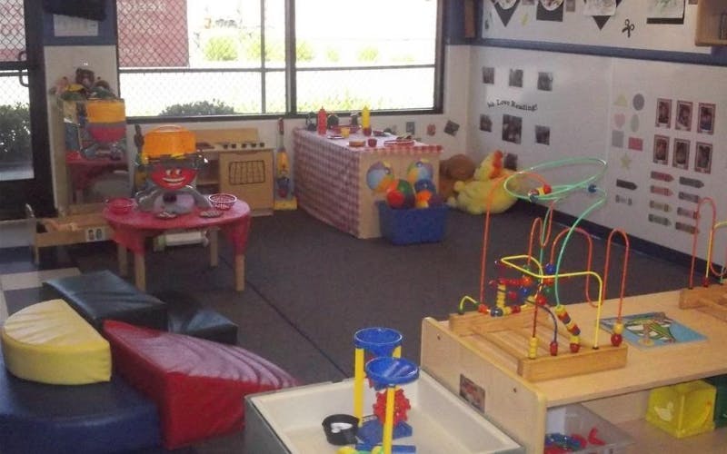 Playroom with small tables, chairs, padded seating, and various toys