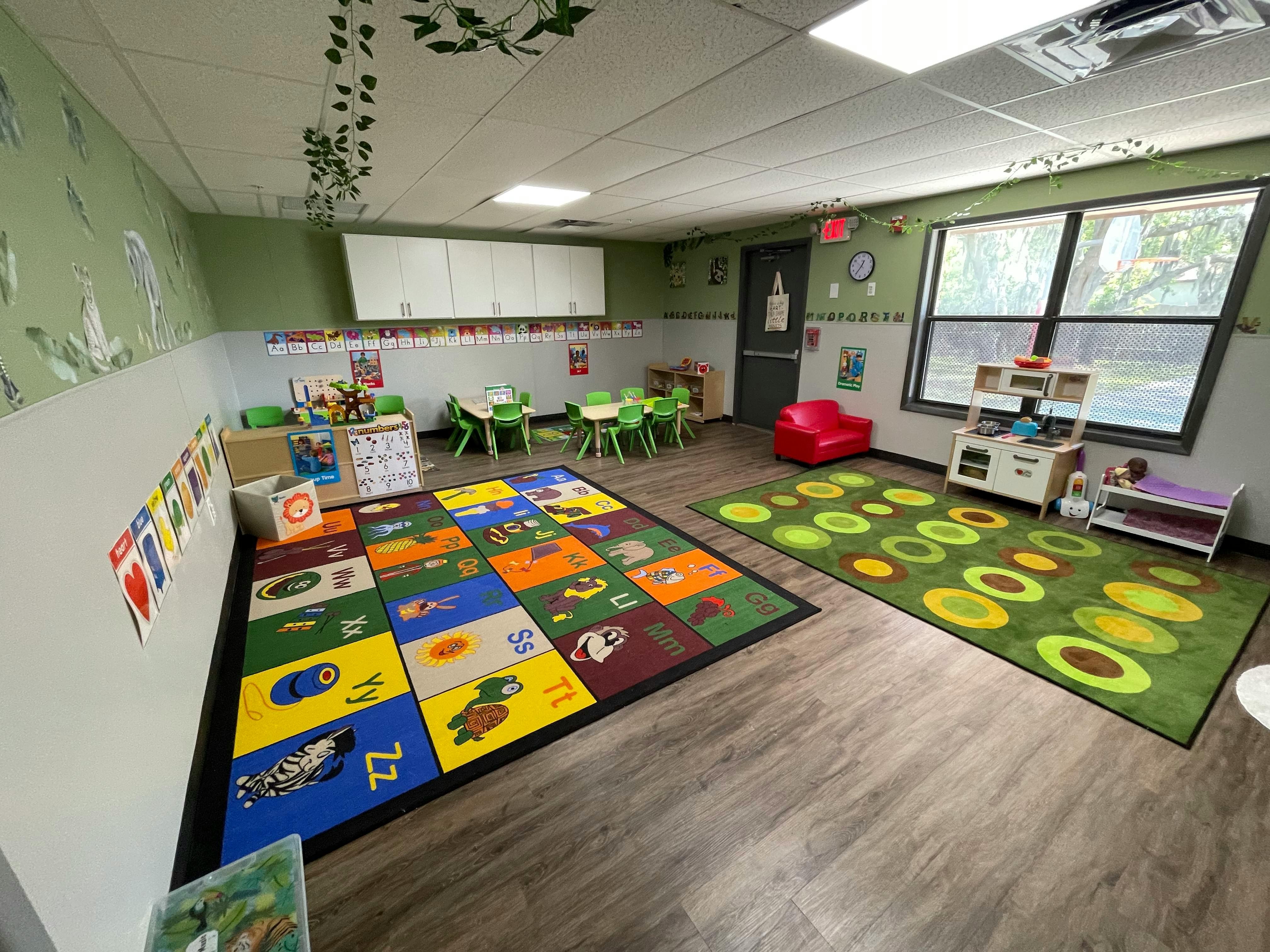 Classroom with colorful alphabet rug, child-sized tables and chairs, play kitchen