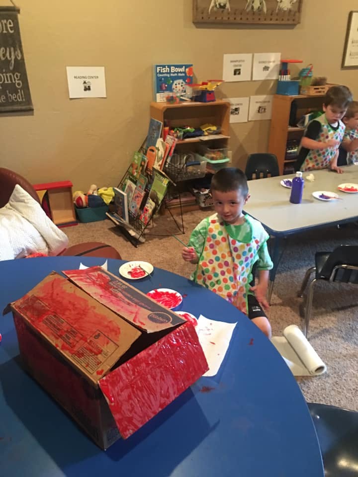 Child in an apron painting a cardboard box red at a table