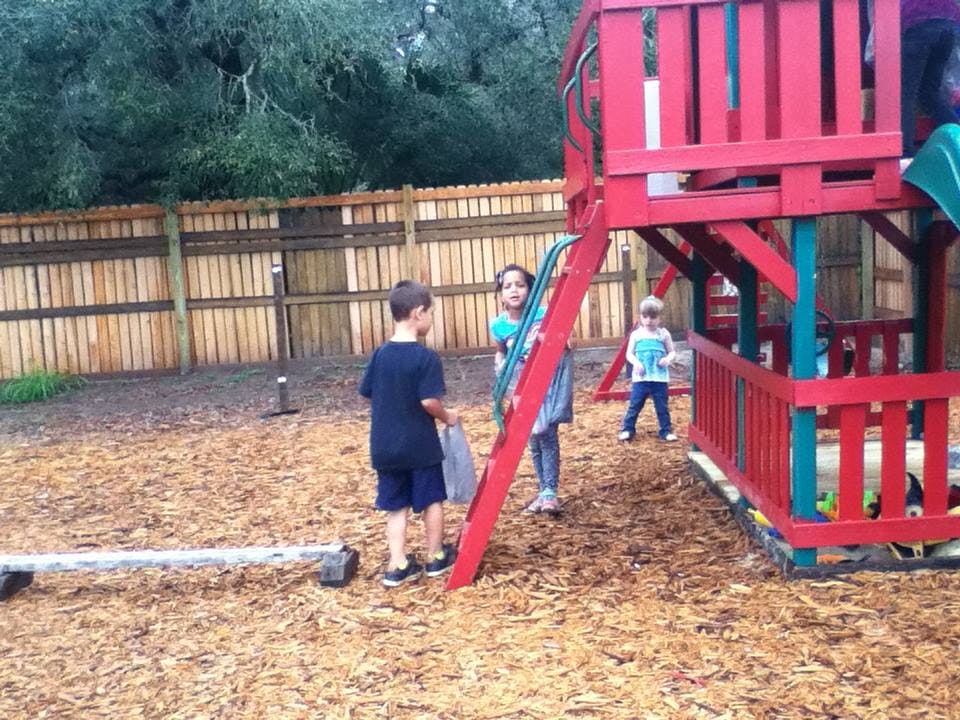 Three children playing on a playground with wood chips