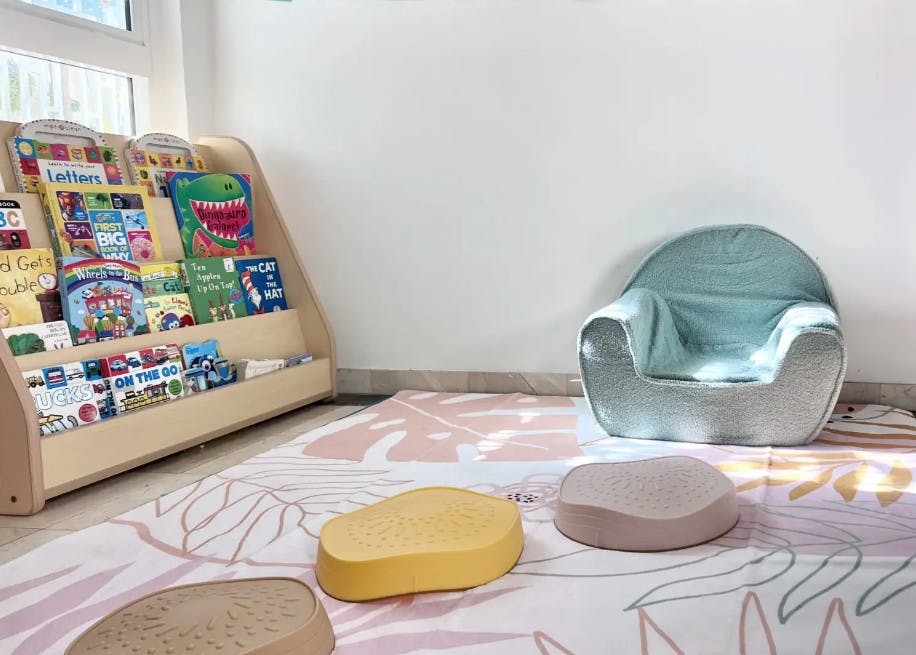 Bookshelf with children's books, small chair, and floor cushions on a rug