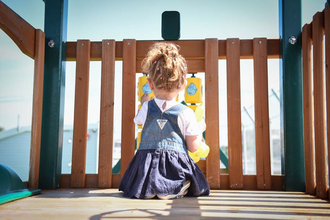 Child in a denim dress sitting on a wooden playground structure