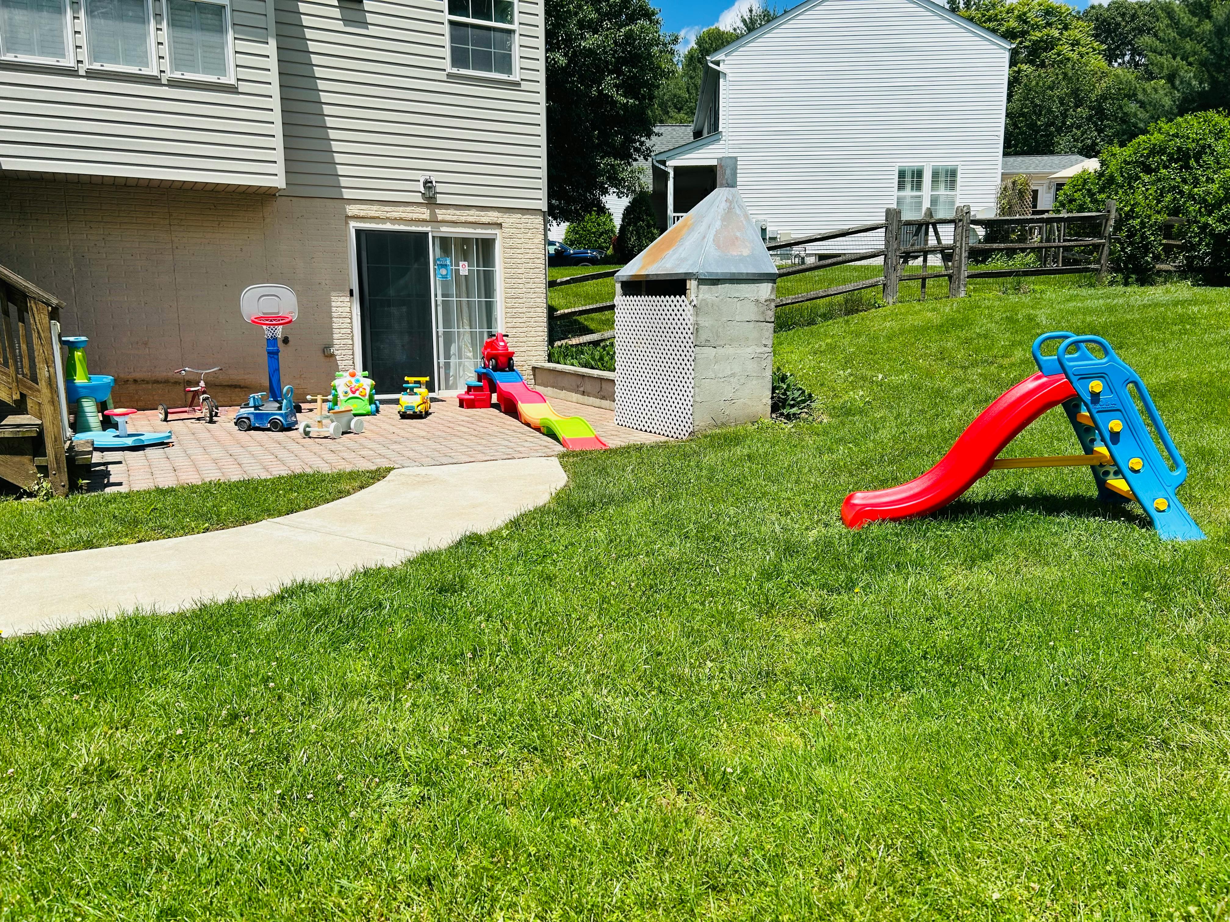 Backyard with a patio, children's toys, and a red and blue slide on the grass