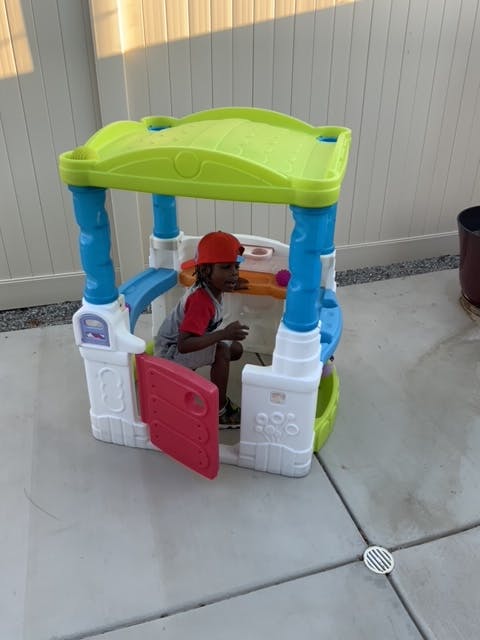 Child in a red hat sitting inside a colorful playhouse
