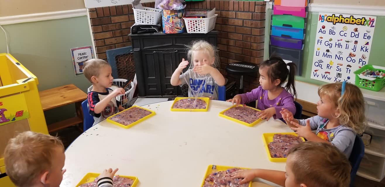 Children sitting around a table with trays of material