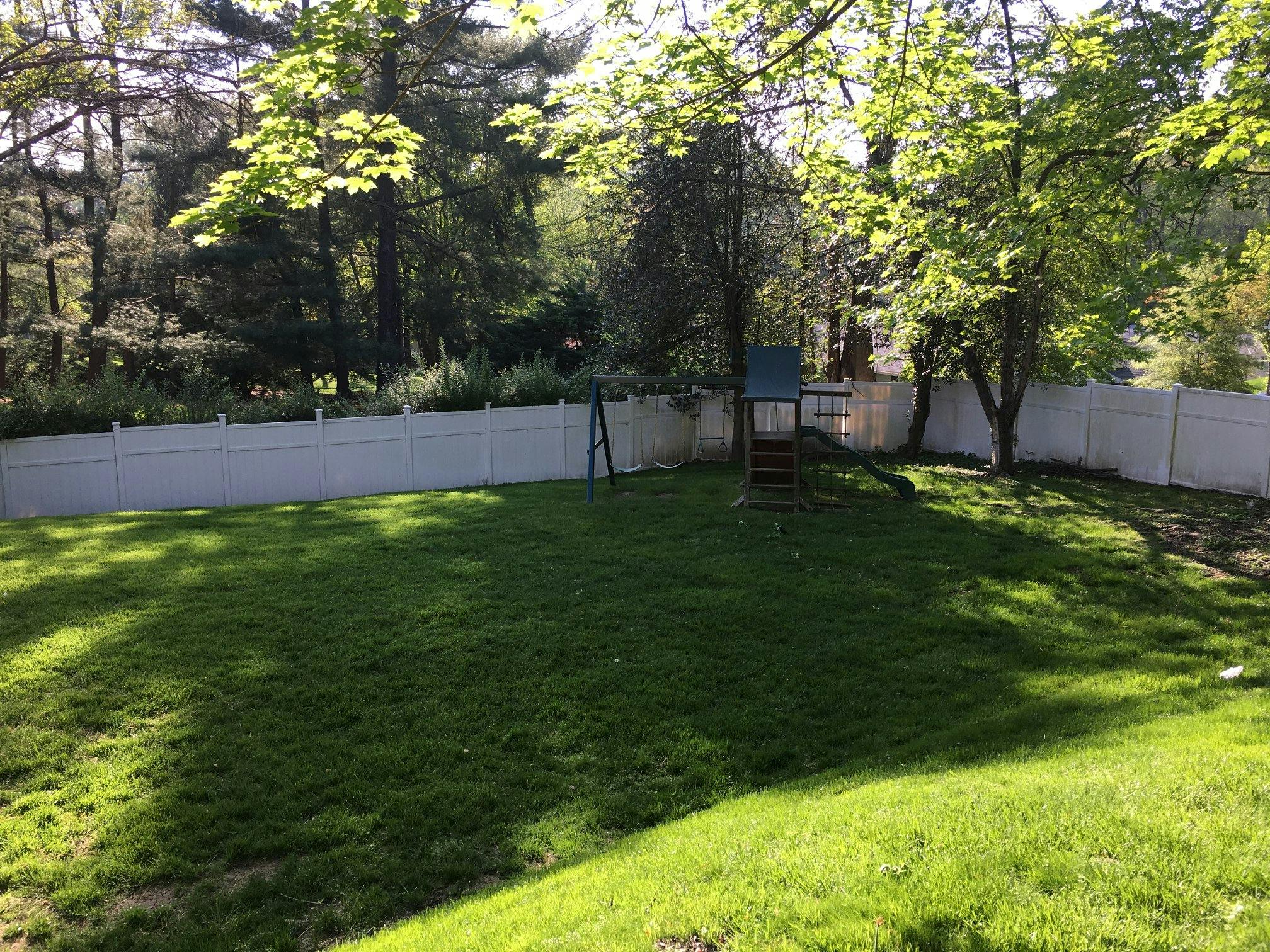Grassy backyard with a white fence and a small play structure