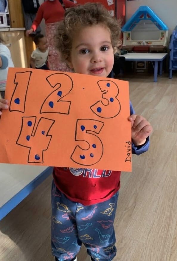 Child holding up an orange paper with numbers 1, 2, 3, 4, 5 with blue dots