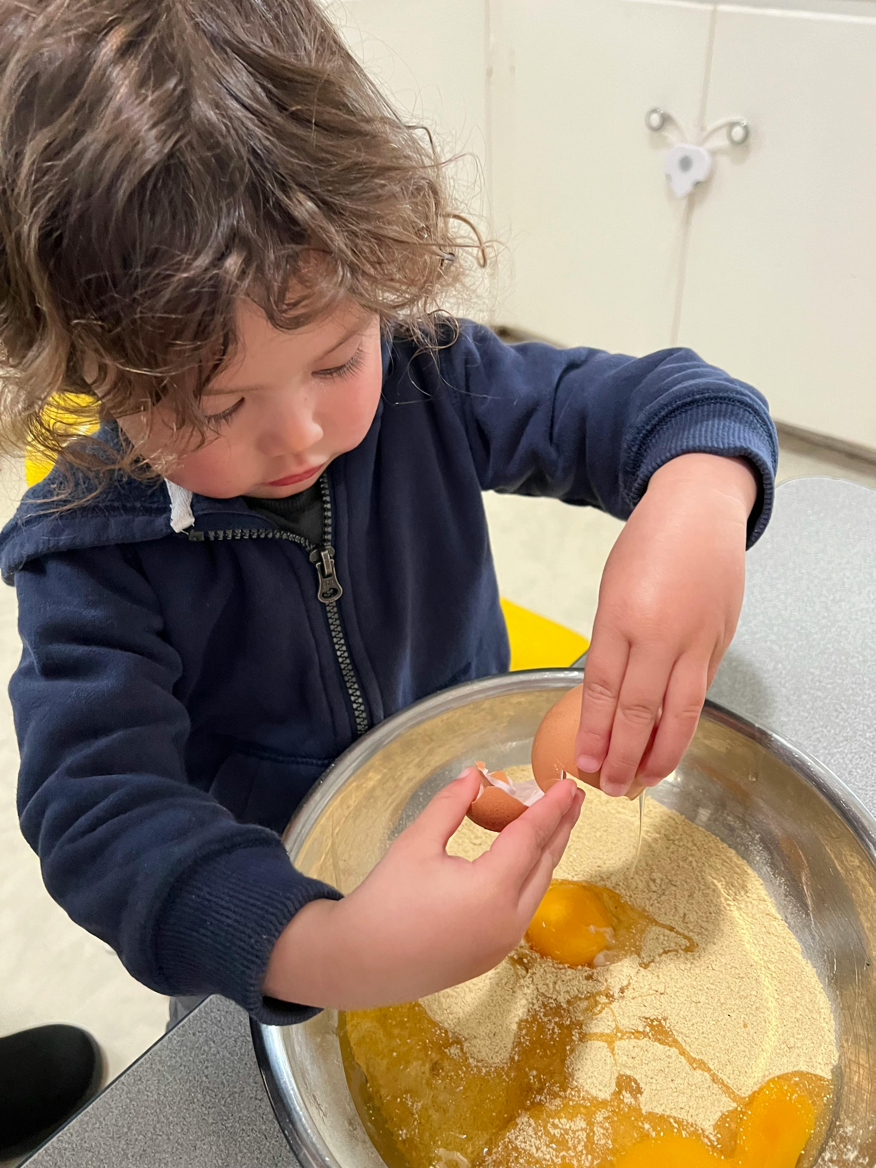 Child cracking an egg into a bowl of ingredients