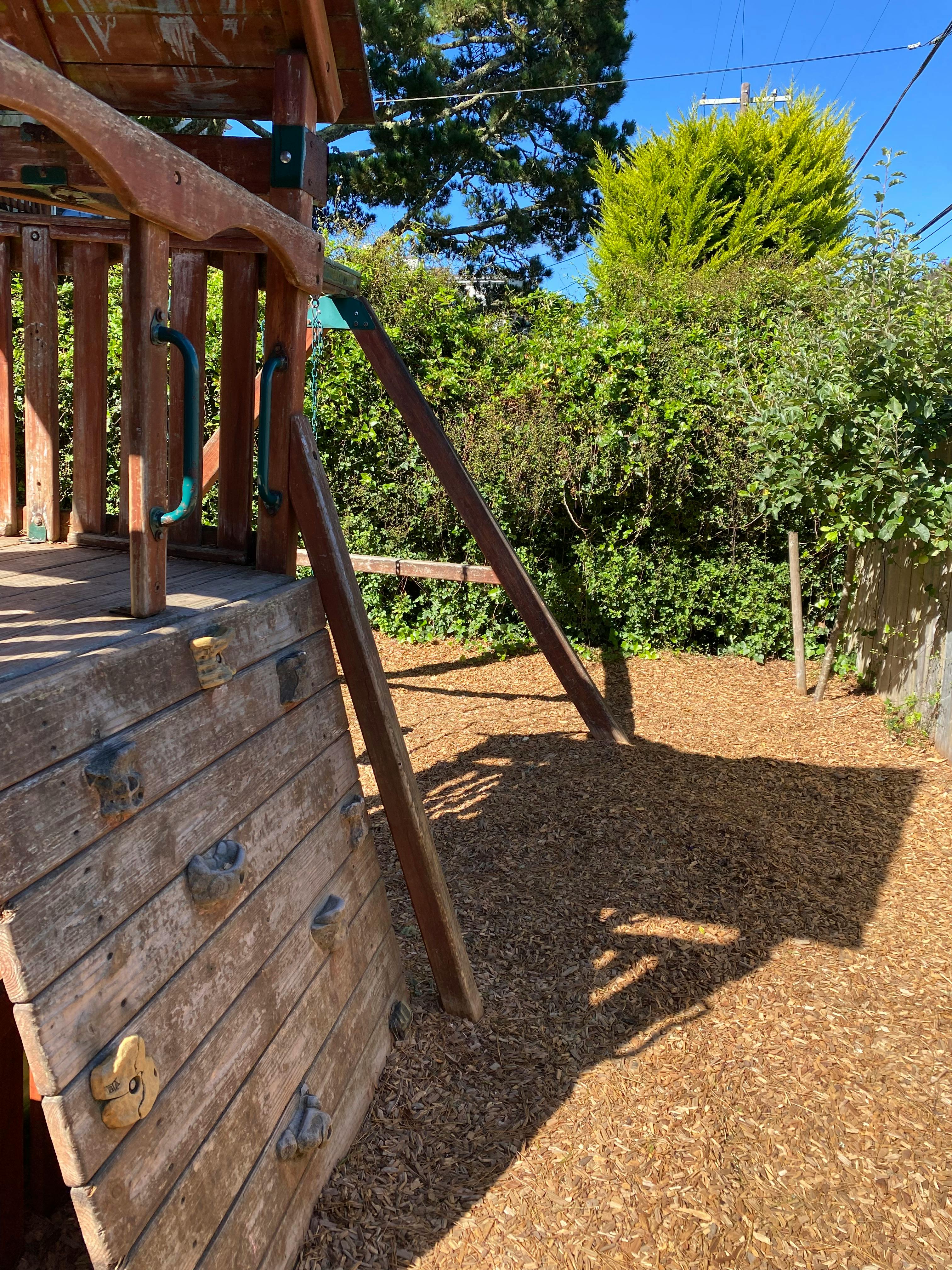 Wooden playground structure with a climbing wall and wood chip ground cover