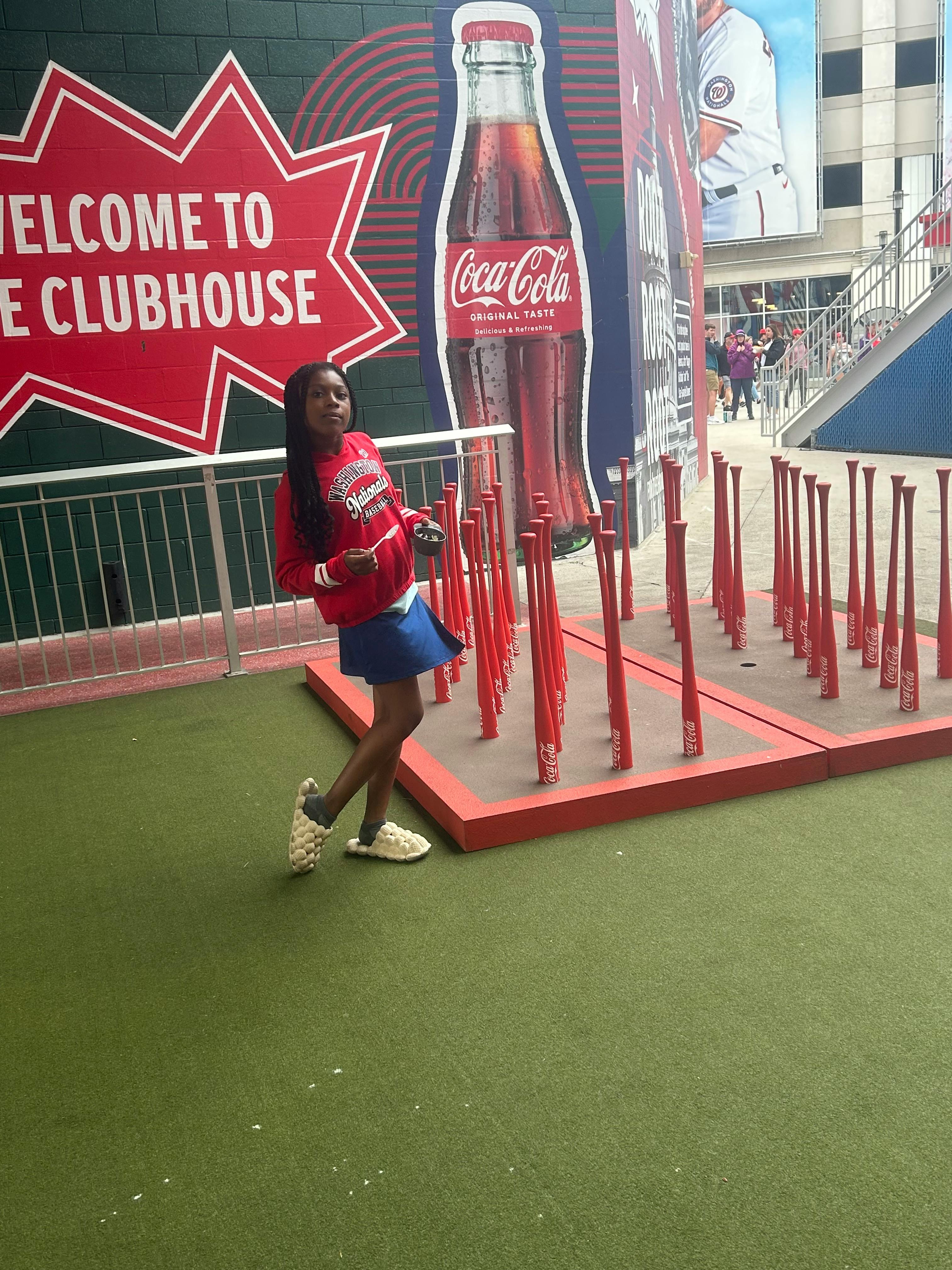 Child standing next to a display of red baseball bats and a Coca-Cola bottle