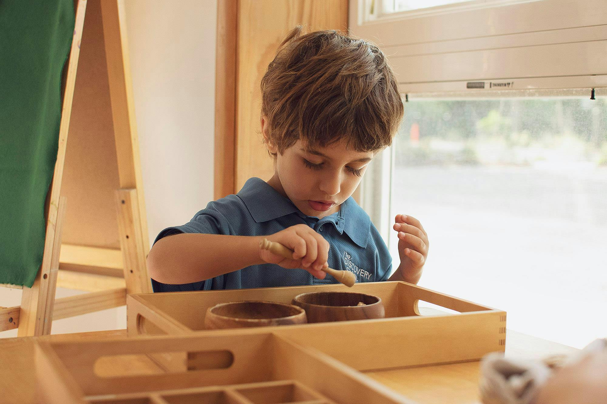 Child playing with small wooden bowls and a spoon in a tray