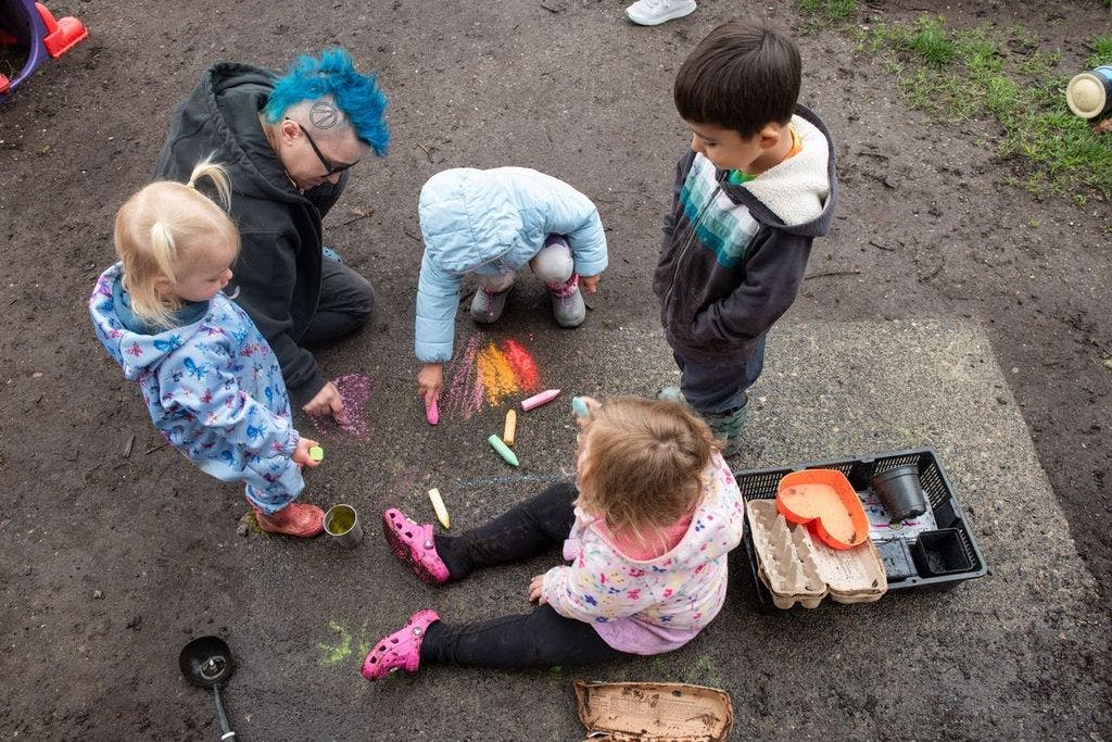 Person and three children drawing with chalk on the ground