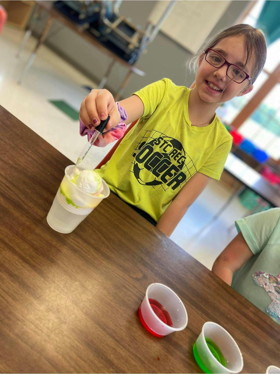 Child in glasses using a dropper over a cup with white contents