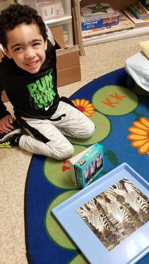 Child kneeling on a rug with a game and a tray with a picture of zebras