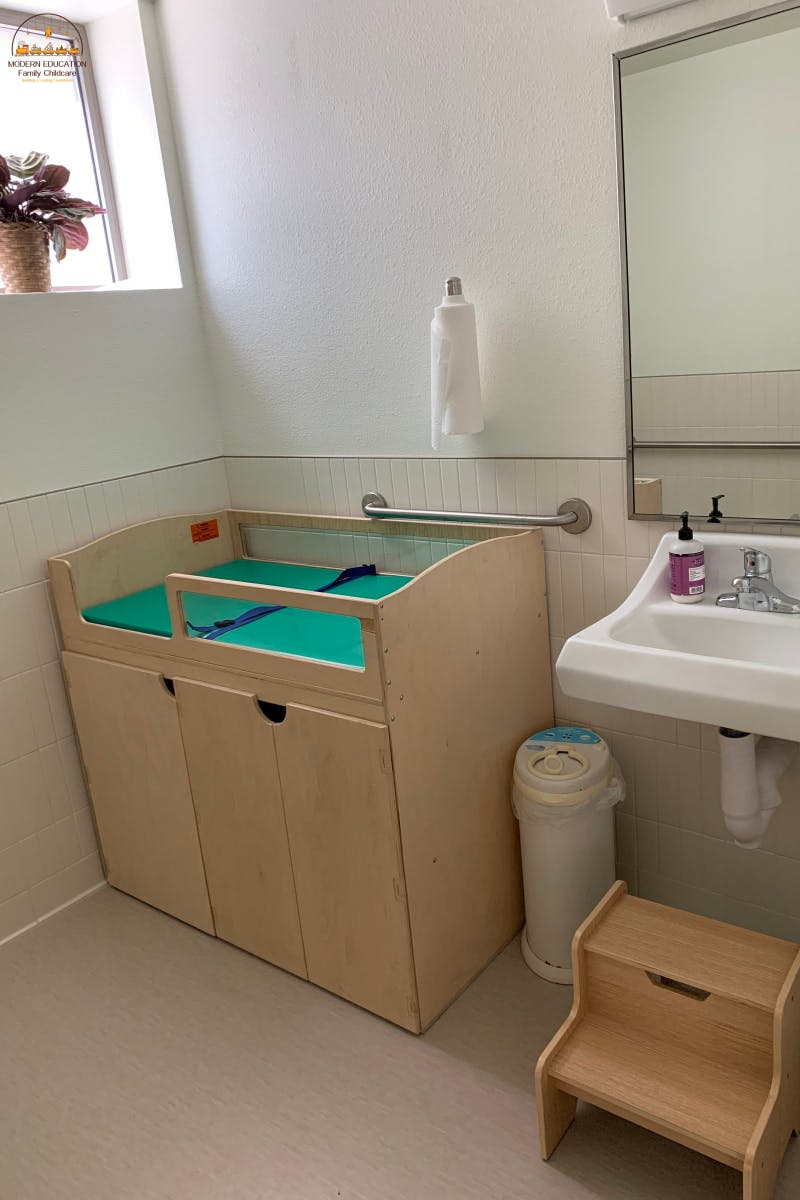 Changing table with green pad and blue straps next to a sink and mirror