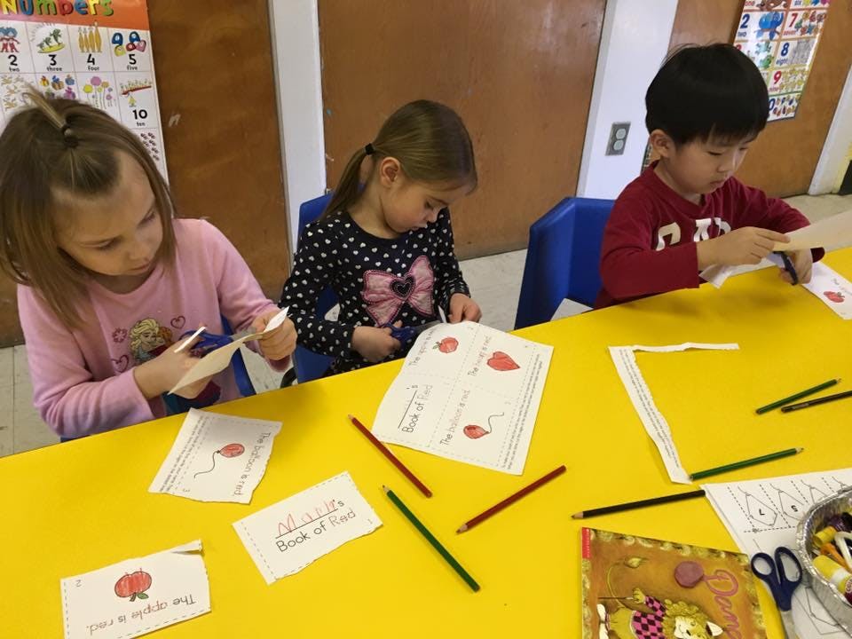 Three children sitting at a yellow table doing crafts